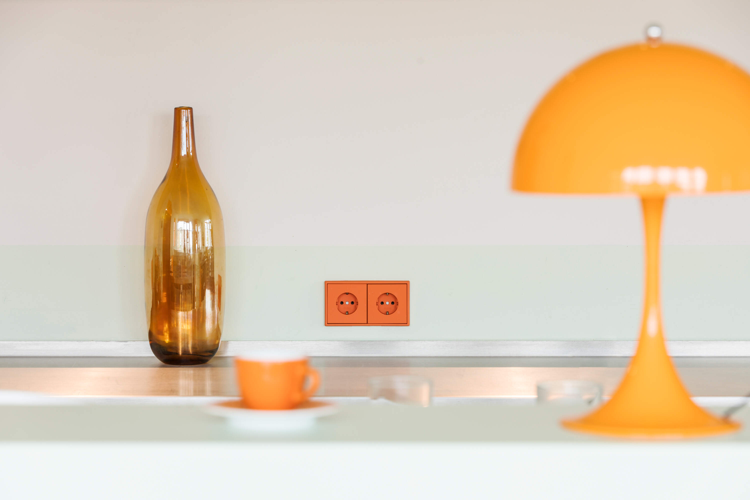 Jung LS gaismas slēdzis oranžā krāsā un uz galda galda lampa un stikla pudele